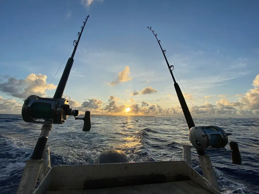 Canne da pesca a poppa di una barca, al sorgere del sole